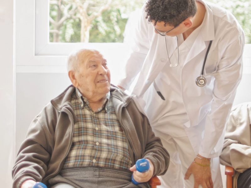 Doctor assisting senior man with exercises in a sunlit room